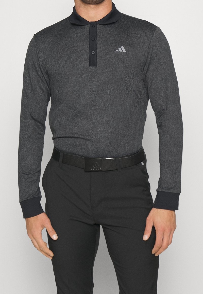 Polo gris à manches longues avec une finition texturée, col noir et patte de boutonnage à trois boutons. Présente un logo Adidas sur la poitrine. Assorti à un pantalon noir.
