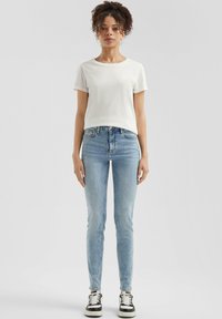 Biała koszulka z podwiniętymi rękawami w zestawie z jasnoniebieskimi obcisłymi dżinsami i czarnymi trampkami. Prosty design, lekki materiał i swobodny krój.