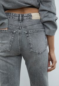 Svetlosivi, visoko krojeni traper hlače z teksturiranim denim zaključkom, ki imajo dve zadnji žepi in blagovno znamko na pasu.