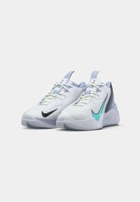 Par de zapatillas deportivas blancas con swooshes de Nike en azul claro y negro, talón texturizado y cordones blancos sobre un fondo liso.