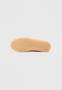 Hellerosa Sohle eines Sportschuhs mit einem strukturierten, wellenförmigen Muster. Das Griffdesign besteht aus einem hellbraunen Gummimaterial für besseren Halt.