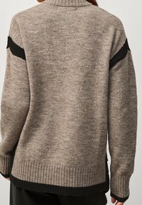 Pull en tricot marron avec des accents noirs sur les épaules, des poignets côtelés et un ourlet. Texture douce et coupe ample avec des fentes latérales pour le confort.