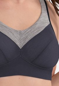 Marineblauwe sportbeha met een gestructureerd mesh-design, voorzien van een lichtgrijze, gemêleerde V-vormige halslijn en gladde bandjes.