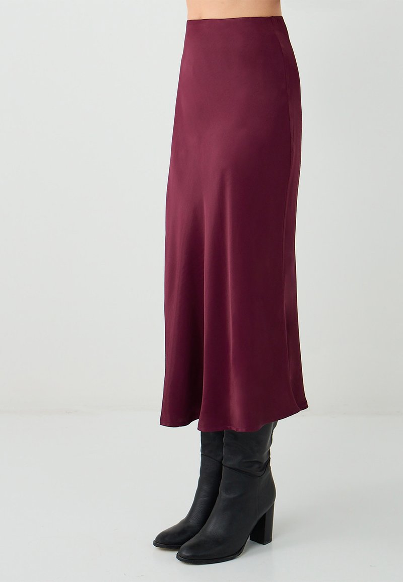 Gonna midi in satin bordeaux con una texture liscia, una vita alta e una silhouette fluida, abbinata a stivali neri con tacco.