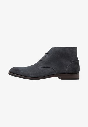 Bottines en suède gris avec un bout étroit, des accents cousus, deux œillets pour les lacets et un petit talon rectangulaire en bois.