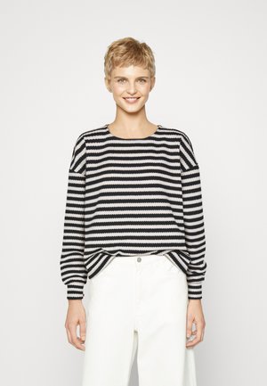 Black and white striped sweater with long sleeves, round neckline, and ribbed texture; paired with white trousers.