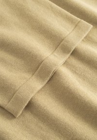 Gros plan sur un tissu tricoté beige avec un poignet cousu, montrant les détails de la texture et des coutures.