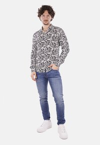 Camicia a maniche lunghe in bianco e nero con un motivo, dalla vestibilità ampia, abbinata a jeans blu slim-fit e sneakers bianche. Collo semplice e senza bottoni.