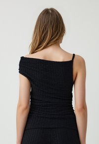 Zwarte textuur top met een off-shoulder ontwerp, voorzien van geplooid materiaal, dunne bandjes en een aansluitende silhout. 