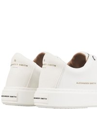 Sneaker bianche in pelle con finitura testurizzata, marchio dorato sul tallone e suola spessa bianca. Design minimalista con punta tonda.