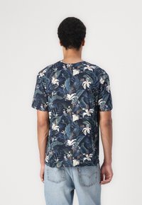 Tricou cu mânecă scurtă, de culoare bleumarin, cu un model floral tropical ce include crini albi și frunze verzi. Material moale, cu o croială lejeră.