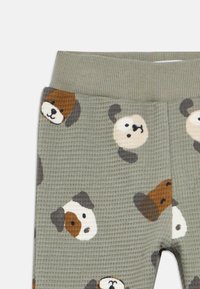 Grønne, teksturerede pyjamasbukser med et gentaget mønster af tegneseriestil hundeansigter i brune, creme og grå farver.