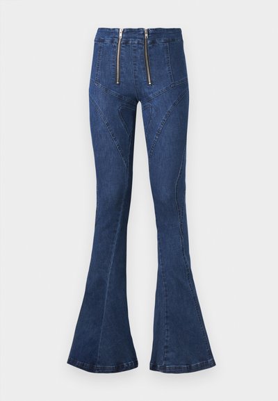 Visoke tamnoplave traperice s razrezom, s dvostrukim patentnim zatvaračem sprijeda, s detaljima zakrivljenih šavova i glatkom teksturom trapera.