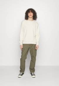 Suéter crema con puños acanalados, combinado con pantalones cargo oliva que cuentan con bolsillos laterales. Lleva zapatillas negras y blancas.