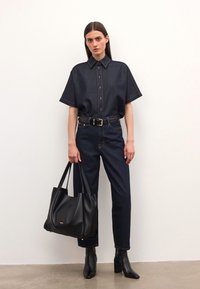 Camisa de manga corta de mezclilla oscura con botones en el frente, combinada con jeans oscuros. Incluye un bolso tote de cuero negro y botas de tobillo.