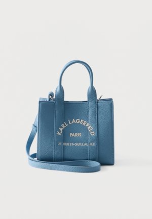 Pequeño bolso de cuero azul con dos asas y correa para el hombro, con texto "Karl Lagerfeld Paris" y dirección en el frente.
