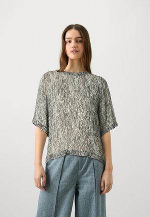 Durchsichtige, locker sitzende Bluse in einem hellen Grau mit schwarz gesprenkeltem Muster. Mit rundem Ausschnitt und kurzen Ärmeln. Kombiniert mit weit geschnittenen Denimhosen.