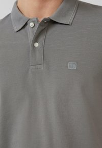 Grijze polo gemaakt van gestructureerde stof met een knoopjessluiting van twee knopen en een klein geborduurd logo. Korte mouwen en een klassiek getailleerd ontwerp.