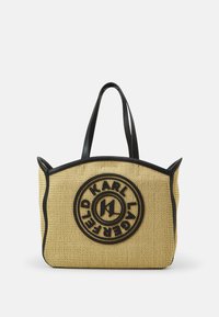 Sac fourre-tout tissé jaune, avec des anses et des finitions en cuir noir, un design de logo circulaire à l'avant, et une forme structurée.