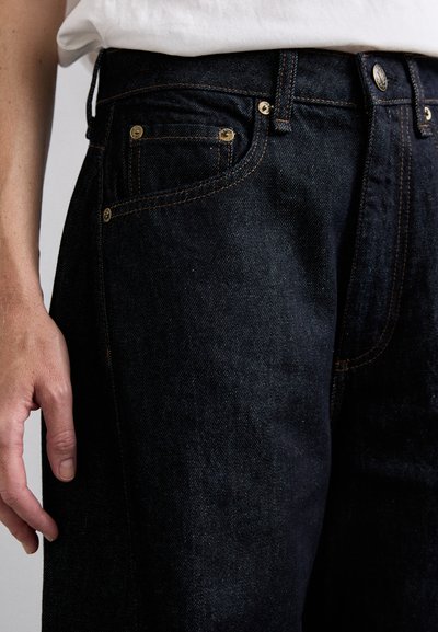Dark blue denim jeans with a smooth texture, featuring gold hardware, double stitching, and classic five-pocket design.