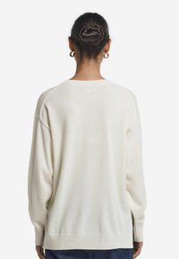 Cremfarbener oversized Pullover mit langen Ärmeln, geripptem Saum und Ärmelbündchen, der eine weiche Textur und ein minimalistisches Design aufweist.