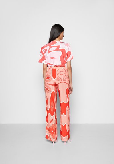 Top com padrão rosa e vermelho, com mangas curtas, combinado com calças largas nas mesmas cores e design, apresentando uma cintura elástica.