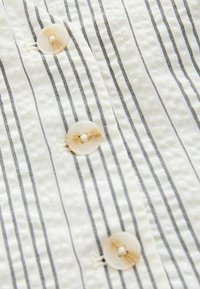 Witte stof met zwarte horizontale strepen en een subtiele textuur, met een duidelijke knop met een gestikte detail.