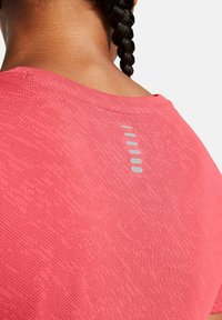 Różowa koszulka sportowa wykonana z teksturowanej tkaniny, z okrągłym dekoltem i odblaskowym akcentem na plecach z poziomymi liniami.