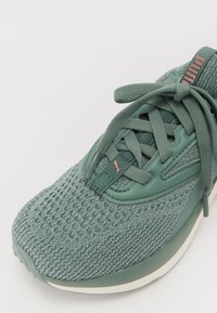 Scarpa da ginnastica verde con tomaia in rete, dettagli testurizzati, lacci abbinati e suola più chiara a contrasto. Presenta il logo vicino ai lacci.