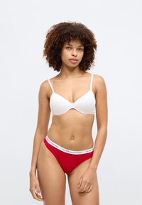 Λευκό μαλακό σουτιέν με ρυθμιζόμενες τιράντες, σε συνδυασμό με κόκκινες εσώρουχες που διαθέτουν λευκή λωρίδα με επωνυμία. Απαλή υφή, απλός σχεδιασμός.