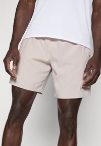 Ανοικτό μπεζ μαγιώ από λείο ύφασμα. Διαθέτει ελαστική μέση και μια μικρή λεπτομέρεια λογοτύπου στο αριστερό πόδι.