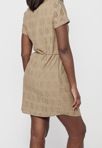 Abito beige a maniche corte con un design testurizzato e motivi a taglio, vita stretta e orlo a livello del ginocchio, realizzato in tessuto leggero.