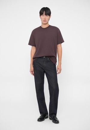 Mörkröd t-shirt med kort ärm i kombination med mörk denimjeans. Jeansen har en rak passform. Modellen står mot en enfärgad vit bakgrund.