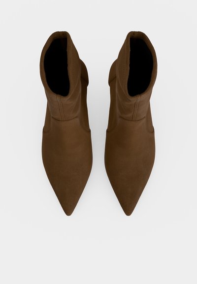 Paire de bottines marron à bout pointu vues de dessus sur un fond clair uni.