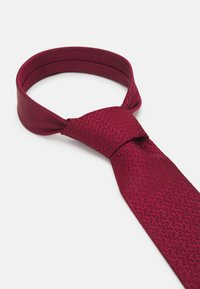 Cravat burgund cu un model texturat, având o finisare netedă și o formă clasică. Design legat cu un bandaj asortat.