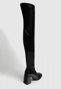 Vysoká černá kožená bota na blokovém podpatku, zaoblená špička a hladký povrch, stojící vzpřímeně na jednoduchém světlém pozadí.