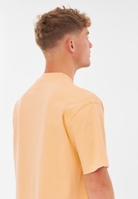 Korte mouwen t-shirt in een zachte oranje stof met een ronde hals, een ontspannen pasvorm en zichtbare stiksels langs de naden. Achteraanzicht weergegeven.