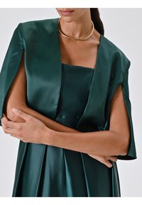 Abito in satin verde smeraldo con una scollatura quadrata strutturata e maniche larghe e fluide. Presenta pieghe sottili e una superficie liscia.