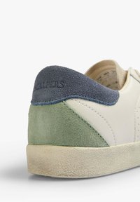 Baskets en cuir blanc avec un talon en daim vert et bleu marine. Semelle extérieure en caoutchouc texturé. Présente des coutures et un logo embossé à l'arrière.