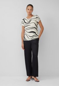 Top a maniche corte color crema con motivo a onde nere, abbinato a pantaloni a gamba larga neri. Tessuto morbido con una vestibilità rilassata.