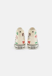 Baskets montantes en toile couleur crème avec des patchs colorés variés, des accents noirs et une semelle en caoutchouc arborant la marque "Converse All Star".