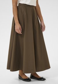 Gonna marrone di lunghezza media con una silhouette ampia, realizzata in tessuto leggero. Abbinata a scarpe nere basse con un'applique a fiocco.