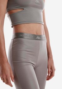 Top corto sportivo grigio con ritagli e leggings a vita alta coordinati, realizzati in tessuto liscio ed elasticizzato. Presenta una vita decorata con il logo.