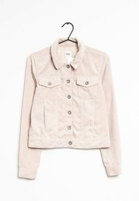 Vaaleanbeige corduroyliekkitakki pitkillä hihoilla, napitettava etuosa, kaulus ja kaksi läpällistä rintataskua, roikkuu mustassa vaatetelineessä.