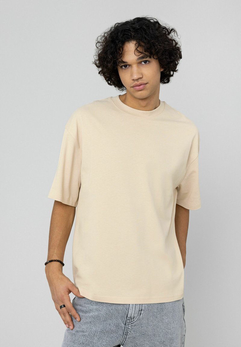 T-shirt beige en coton à manches courtes, coupe décontractée, encolure ronde et texture lisse. Associé à un short en jean gris clair.