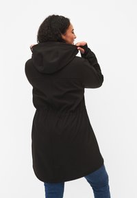 Zwarte softshell jas met capuchon, cinched taille, lange mouwen en zijzakken. Soepele textuur en een strakke, minimalistische stijl.