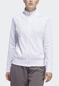 Casaco branco com fecho zip em tecido texturizado, com gola alta e bolsos laterais, combinado com calças cinzas. Apresenta uma frente lisa e punhos canelados.
