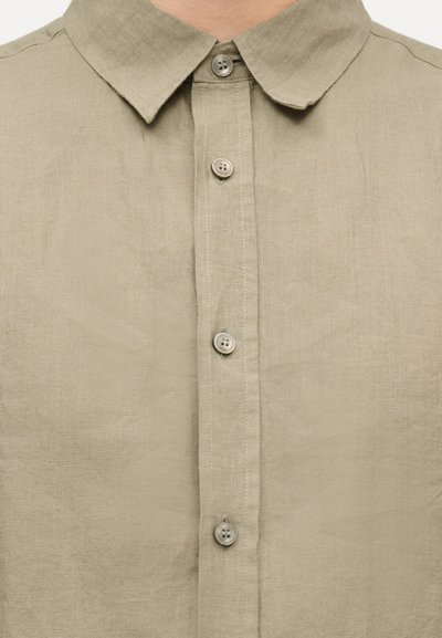 Μπεζ λινό πουκάμισο με κλασικό γιακά και τέσσερα εμφανή στρογγυλά κουμπιά στην πρόσοψη.