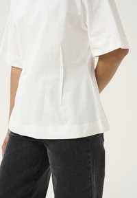 Witte katoenen blouse met een loose fit, met zijsplits en korte mouwen, gecombineerd met zwarte denim broek met een subtiele textuur.