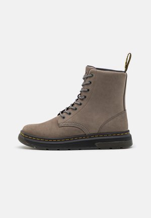 Bottines en suède gris avec semelle en caoutchouc noir, coutures jaunes, design à lacets et languette à l'arrière pour un enfilage facile.